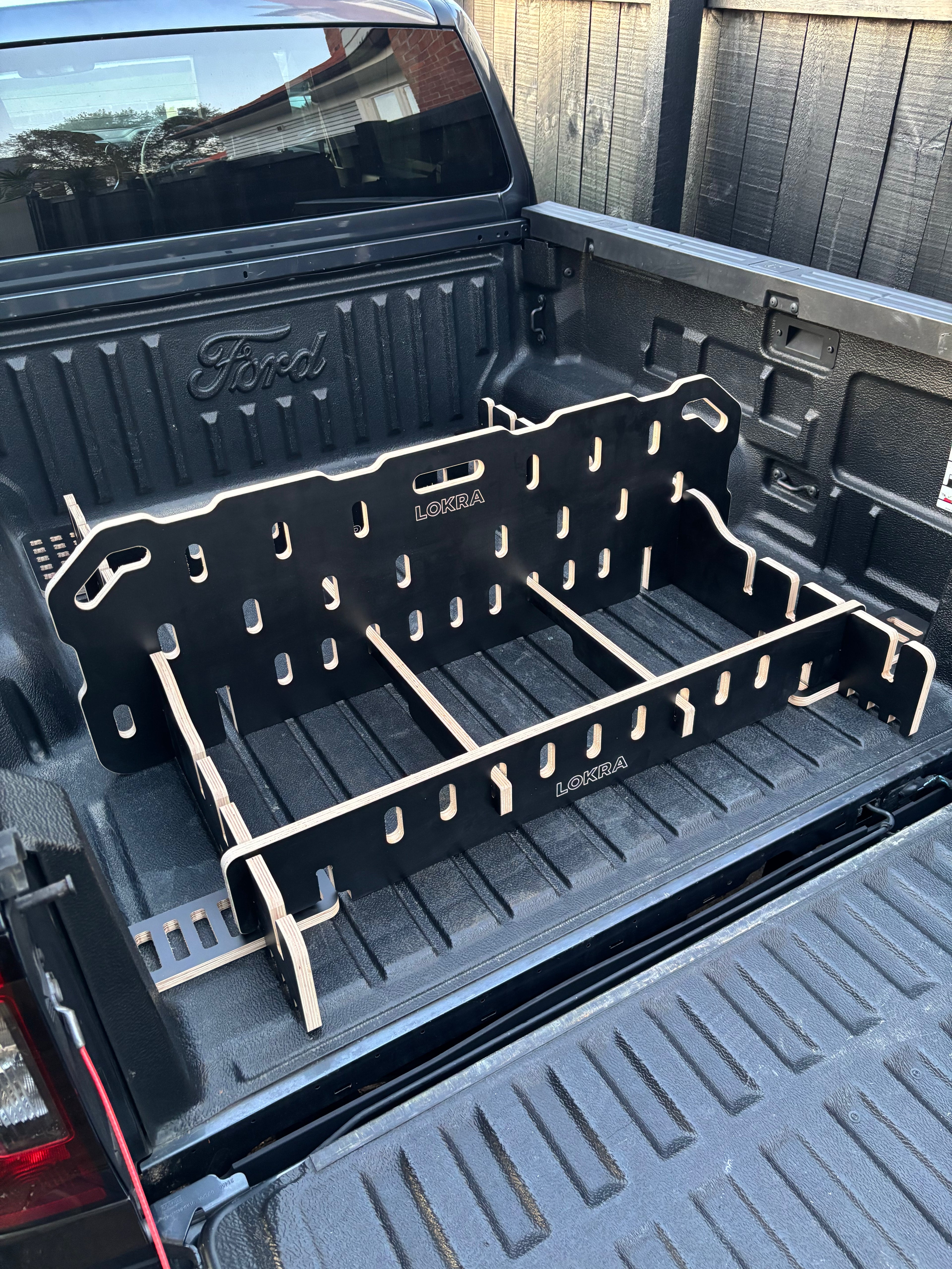 A black plastic truck bed with plywood support bars installed in the bed of a black Ford pickup truck.