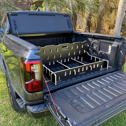 A black LOKRA branded truck bed organizer rack installed inside the bed of a dark pickup truck, shown outdoors with the truck tailgate open and trees in the background.