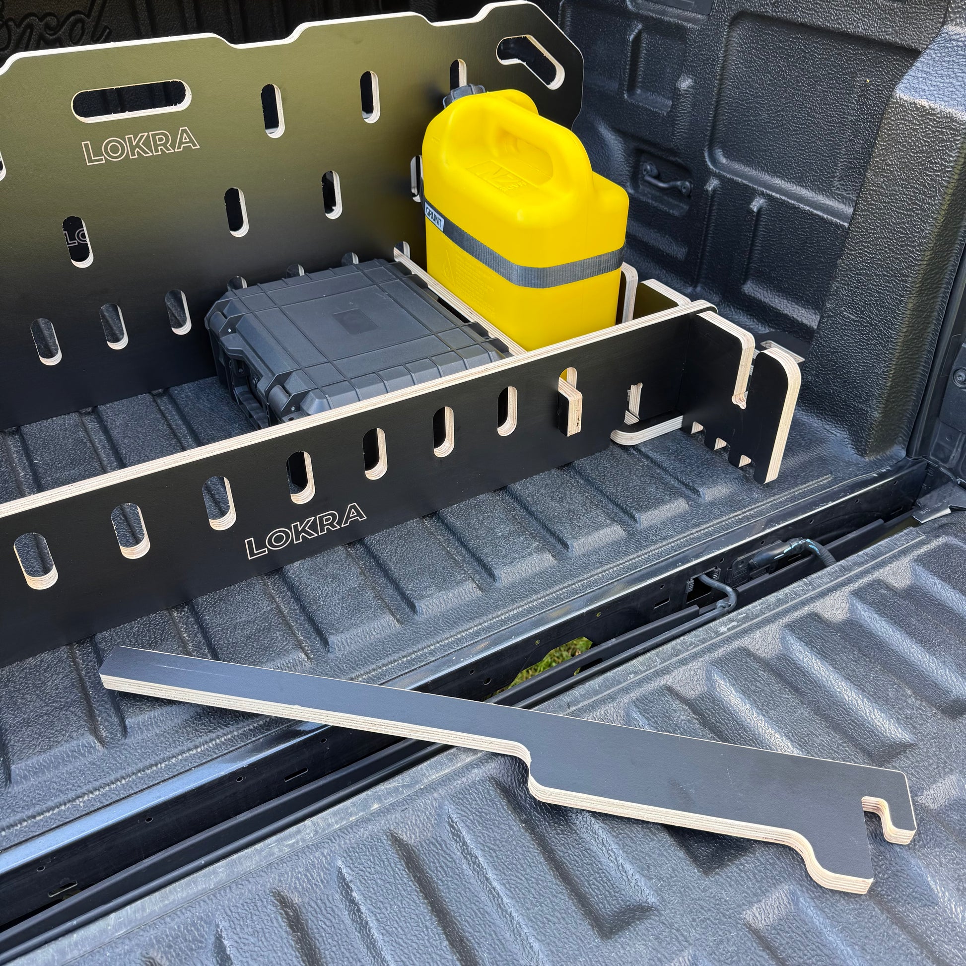 Black LOKRA truck bed organizer rack installed in the bed of a pickup truck, shown with a yellow container, a gray hard case, and a metal tool inside the truck bed.